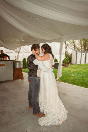 A couple shares their first dance under a white draped tent during an outdoor wedding reception.