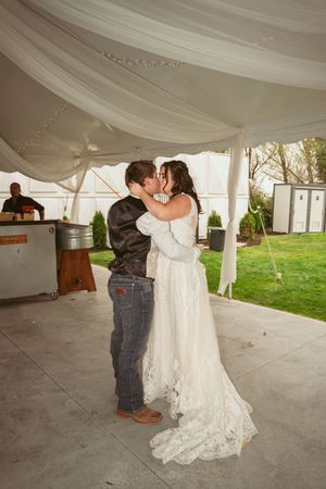 A couple shares their first dance under a white draped tent during their rustic outdoor wedding celebration.
