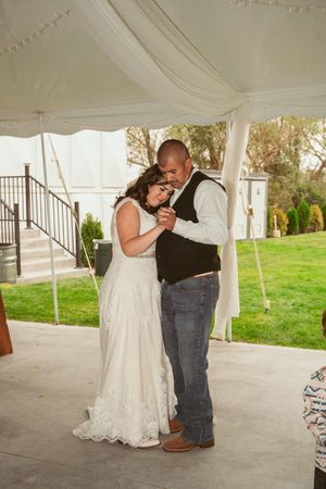 A couple shares a tender dance moment under a white tent canopy with lush green grass visible in the background.