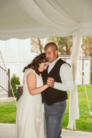 A couple shares an intimate slow dance under a white draped tent during what appears to be a wedding reception.