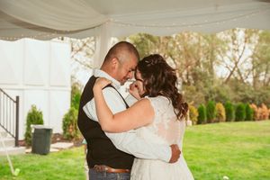 A romantic couple shares their first dance under an outdoor wedding tent on a sunny day.