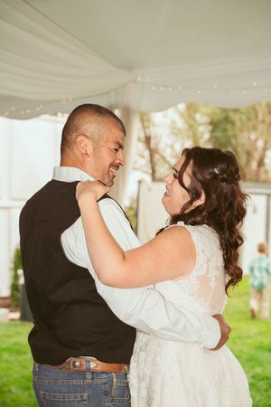 A couple laughs together while dancing beneath white tent draping and twinkle lights at an outdoor event.