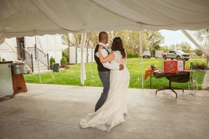 A couple shares their first dance under an outdoor wedding tent on a patio with green lawn and decor visible.