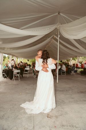 A romantic slow dance moment under elegant white tent draping at an outdoor wedding reception.