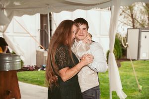 People sharing hugs and embraces during a wedding reception under a white tent.