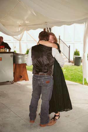 Guests dancing and embracing during a wedding reception on a concrete floor under white tent draping.