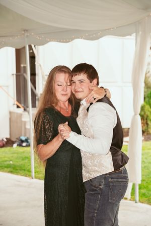 Two people dance together under a white tent canopy at an outdoor event, with one wearing black lace and one in light vest.