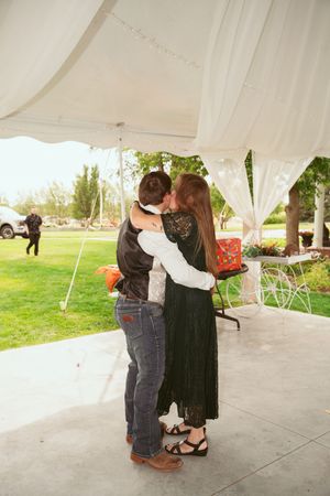 A couple shares a tender embrace under an elegant white tent on a sunny day.