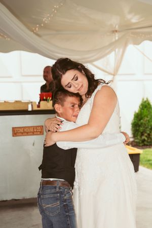 A tender moment captured during a wedding reception with embraces under a white tent canopy.