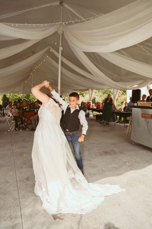 A couple shares their first dance under an elegant tent with flowing fabric draping and sparkling lights at their wedding reception.