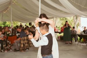 A couple slow dances under white fabric draping at an outdoor wedding reception.