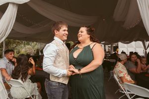 Dancing couples celebrate at an evening wedding reception under draped white fabric and soft lighting.