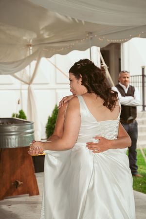 A person in a white wedding dress dances under a draped tent during a reception celebration.