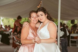 Two people share an emotional embrace while dancing at a wedding reception under a white tent.