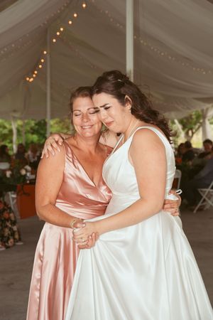 Wedding party members sharing joyful embraces under a tent decorated with string lights.