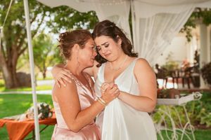 Two people share an intimate moment under a white tent during a wedding celebration outdoors.