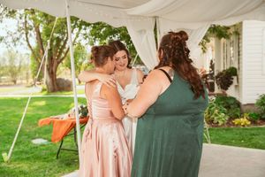 Three guests share an emotional embrace during an outdoor tented wedding reception.