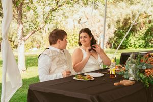 Outdoor wedding reception setup under white tent with rustic wooden tables and floral arrangements.