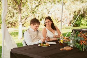 A picturesque outdoor dining scene with candles and greenery decorating a wooden table at sunset.