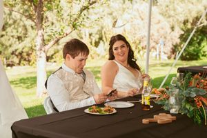 Guests enjoying an elegant outdoor dinner at long wooden tables with greenery and candlelight decorations in a garden setting.