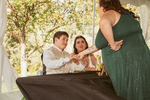 Wedding guests participate in a celebratory game at a sunny outdoor reception under a tent.