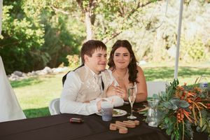 A happy couple shares a tender moment at their outdoor wedding reception table decorated with greenery.
