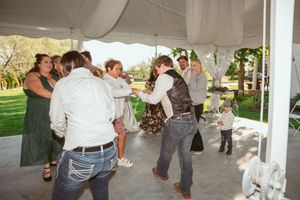Wedding party and guests enjoying a lively dance celebration under a white tent.