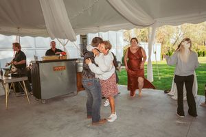 People dancing and socializing under a white tent at an outdoor celebration with a bar setup.