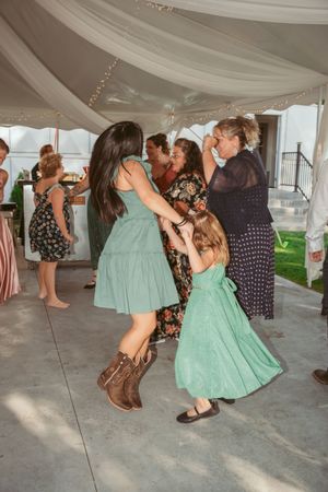 Wedding reception attendees dance and twirl in flowing dresses under a white draped tent canopy.