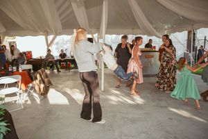 Wedding guests dance joyfully under a draped tent at an outdoor reception celebration.