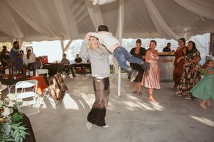 Guests dancing energetically under a white tent during a festive wedding celebration.