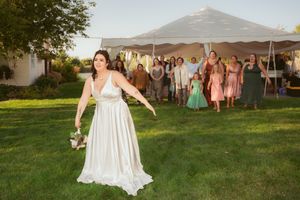 A bride in a white dress prepares to toss her bouquet during an outdoor wedding reception under a tent.