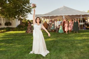 Wedding guests gather on a lush green lawn under a white tent during sunset.