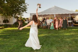 Person in white dress tosses bouquet during traditional wedding moment outdoors under tent.