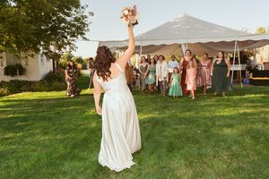 Wedding guests throwing confetti and celebrating on a sunny lawn with white tents in the background.