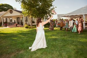 An outdoor wedding celebration with white tents set up on a grassy lawn during golden hour.