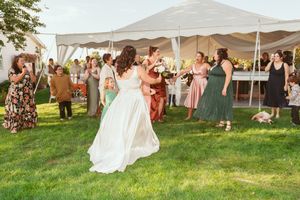 Wedding celebration on green lawn with guests dancing under white tent at sunset.