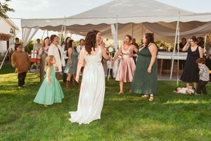 Wedding guests dancing and mingling under a white outdoor tent on a sunny lawn.
