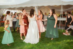 A celebration under a white tent with people in formal attire dancing and socializing on a grassy lawn.