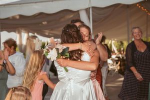 Reception guests dancing and celebrating under a white tent with twinkling lights.