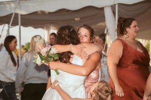 Emotional embraces and hugs during a wedding reception under a white tent canopy.
