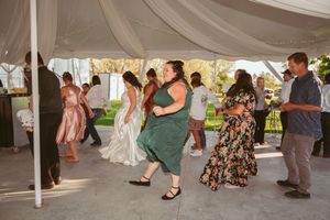 Guests dancing and celebrating under outdoor wedding tent with flowing white fabric decorations.