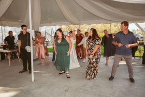 Wedding guests dance and celebrate under a white tent at an outdoor reception.