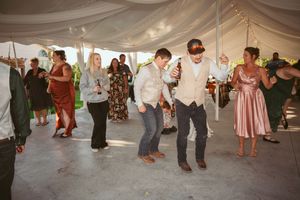 Guests dancing in a line under a white tent at an outdoor wedding reception.