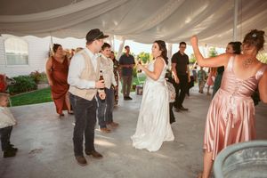 Wedding guests dance and celebrate with the bride and bridesmaids in peach-colored dresses on an outdoor dance floor.