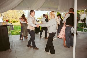 Couples dancing together under a draped white tent at an outdoor reception.