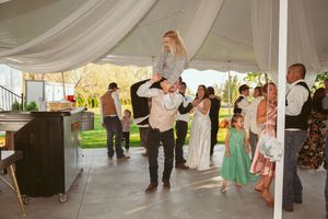 Wedding guests enjoy dancing and celebrations as someone is lifted up during a reception under a tent.