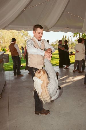 A couple performs an impressive dip dance move under a wedding reception tent on an outdoor dance floor.