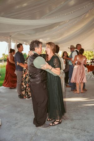 Couples dancing together under an elegant white tent at an outdoor wedding reception venue during daytime.