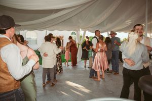 Wedding guests dance and celebrate on the dance floor under draped white fabric at an outdoor reception tent.